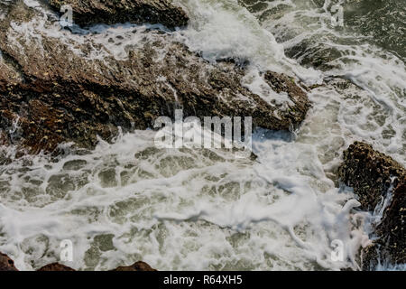 Yarada Strand mit indischen Ozeanwellen, die auf die Uferfelsen und -Steine krachen. Langzeitbelichtung mit seidig glattem Wasser und Felsen im Hintergrund. Stockfoto