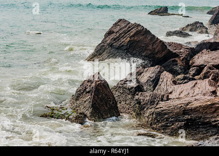 Yarada Strand mit indischen Ozeanwellen, die auf die Uferfelsen und -Steine krachen. Langzeitbelichtung mit seidig glattem Wasser und Felsen im Hintergrund. Stockfoto