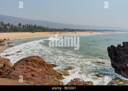 Yarada Strand mit indischen Ozeanwellen, die auf die Uferfelsen und -Steine krachen. Langzeitbelichtung mit seidig glattem Wasser und Felsen im Hintergrund. Stockfoto