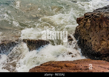 Yarada Strand mit indischen Ozeanwellen, die auf die Uferfelsen und -Steine krachen. Langzeitbelichtung mit seidig glattem Wasser und Felsen im Hintergrund. Stockfoto