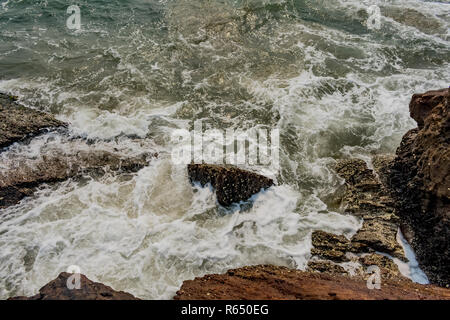 Yarada Strand mit indischen Ozeanwellen, die auf die Uferfelsen und -Steine krachen. Langzeitbelichtung mit seidig glattem Wasser und Felsen im Hintergrund. Stockfoto