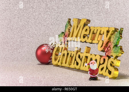 Winzige Figürchen von Santa Claus auf einem Glitzer Silber Schnee Hintergrund mit dem goldenen Worte frohe Weihnachten und ein Christbaumschmuck Kugel mit sn Cute Stockfoto