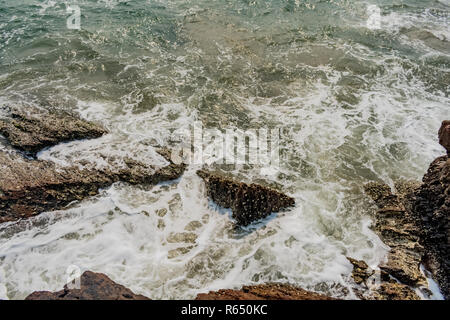 Yarada Strand mit indischen Ozeanwellen, die auf die Uferfelsen und -Steine krachen. Langzeitbelichtung mit seidig glattem Wasser und Felsen im Hintergrund. Stockfoto