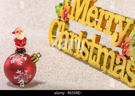 Niedlich winzigen Figürchen von Santa Claus am Weihnachtsbaum Schneeflocken Muster ornament Kugel mit Glitzer Silber Schnee Hintergrund und den goldenen Worten Merr Stockfoto