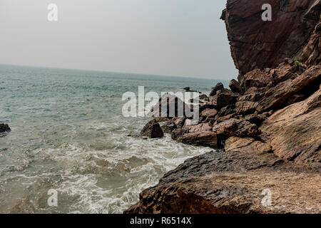 Yarada Strand mit indischen Ozeanwellen, die auf die Uferfelsen und -Steine krachen. Langzeitbelichtung mit seidig glattem Wasser und Felsen im Hintergrund. Stockfoto