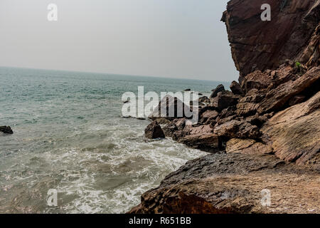 Yarada Strand mit indischen Ozeanwellen, die auf die Uferfelsen und -Steine krachen. Langzeitbelichtung mit seidig glattem Wasser und Felsen im Hintergrund. Stockfoto