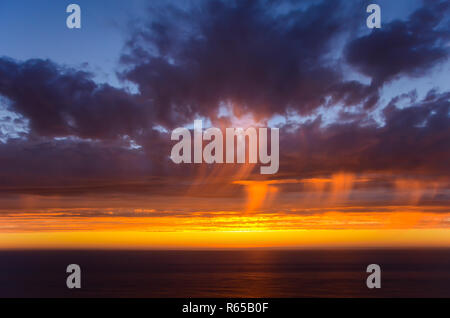 Brilliant orange Sonnenuntergang highlights Streifen von der Regen von lila Wolken über dem Pazifischen Ozean entlang der Kalifornien Big Sur Küste Stockfoto