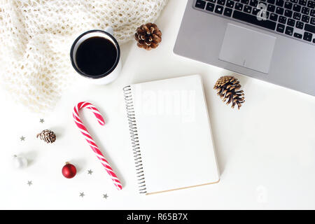 Winter Arbeitsbereich Komposition. Notebook Mock-up-Szene. Tasse Kaffee, Wolldecke, Zuckerstange, Weihnachtsbaumschmuck, Tannenzapfen und Laptop auf weißem Hintergrund. Flach, Ansicht von oben. Blogger Design. Stockfoto