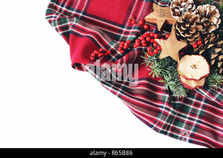 Weihnachten festlich gestaltete Komposition. Winter Blumenschmuck. Tannenzapfen, Fir Tree Branches, rot Stechpalme Beeren und Holz- Sterne und auf Kariert tartan plaid. Weißem Hintergrund. Flach, oben Stockfoto