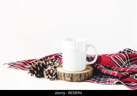 Winter noch leben Komposition. Leere Keramik/mugstanding auf Holz geschnitten, Tannenzapfen und rot kariert tartan plaid auf weißem Hintergrund. Weihnachten im traditionellen Stil Foto, mockup. Stockfoto