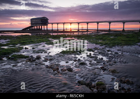 Ein Mann sieht den Sonnenaufgang über Bembridge RNLI Lifeboat station in Lane End Strand auf der Isle of Wight Stockfoto