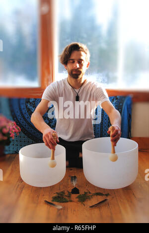 Ein Mann spielt mit seinen zwei Kristall Klangschalen für eine Badewanne meditation Stockfoto