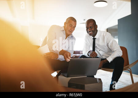 Zwei verschiedene Geschäftsleute lächelnd, während sitzen zusammen in einem Büro diskutieren über ein Laptop Stockfoto