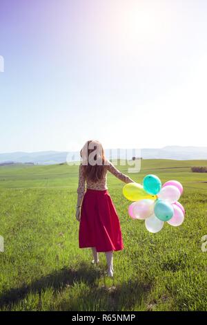 Happy girl In den Wiesen der Toskana mit bunten Luftballons, gegen den blauen Himmel und grüne Wiese. Toskana, Italien Stockfoto