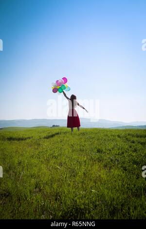 Happy girl In den Wiesen der Toskana mit bunten Luftballons, gegen den blauen Himmel und grüne Wiese. Toskana, Italien Stockfoto