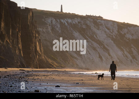 Ein Mann, der seinen Hund bei Sonnenaufgang am Yaverland Strand auf der Isle of Wight, Großbritannien Stockfoto