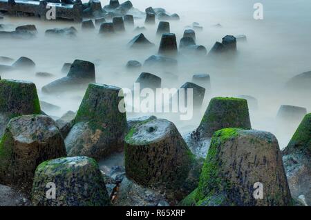 Ein Felsvorsprung Küstenschutz Barriere aus Tetrapods und großen Felsen in grün Moos bedeckt. Stockfoto