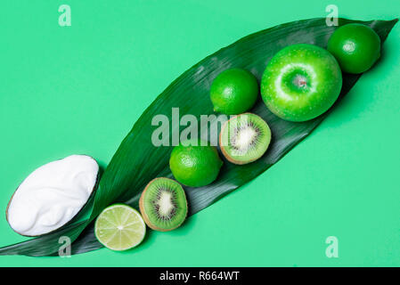 Oben Ansicht eines grünen Tisch mit einer Mischung aus grüne Früchte, Äpfel, Kiwi, Limes auf einem großen Blatt und Joghurt. Im minimalistischen Stil. Das gesunde Essen. Veganes essen. Stockfoto