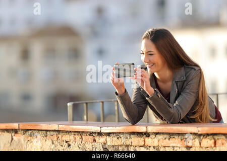 Glückliche Frau Aufnehmen von Videos oder Fotos mit Smart Phone in einem Balkon bei Sonnenuntergang Stockfoto