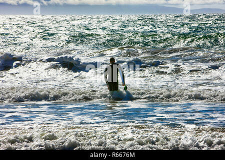 Silhouette eines Mannes zu seinem Surfbrett in den Pazifischen Ozean bei hendry's Beach in Santa Barbara, CA Stockfoto