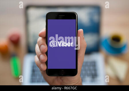 Ein Mann schaut auf seinem iPhone die zeigt die Viber logo, während saß an seinem Computer Schreibtisch (nur redaktionelle Nutzung). Stockfoto