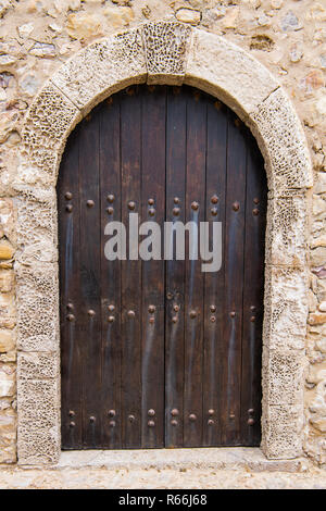 Rustikale gewölbten Holz Tür mit verrosteten Schraubenköpfe abgerundet und Coral Stone Verkleidung in einer Steinmauer am Cabo de Sao Vicente in Portugal Stockfoto