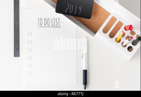 Ansicht von oben zu tun2019 Papier Hinweis auf moderne Büro Schreibwaren auf der weißen Liste Tabelle. Bleistift, Notizblock, Stift, Lineal und Bleistift Box mit Anlage. Mock up Papier Hinweis Stockfoto