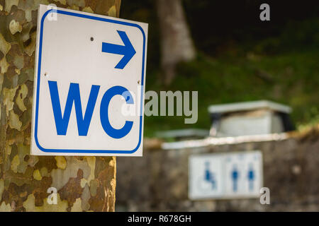 Weißes Schild an einem Baum, wo es WC geschrieben ist angefügt Stockfoto