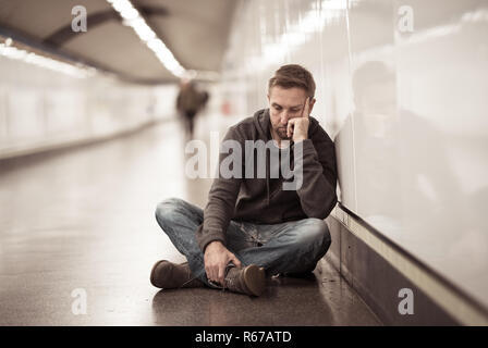 Traurige junge Mann weinen leiden Depression stress sitzen auf dem Boden Street U-Bahn Tunnel suchen verzweifelt lehnte sich an der Wand allein in der psychischen Störung Emo Stockfoto