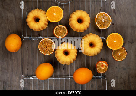 Kleine orange bundt Kuchen mit frischen und trockenen Orangen auf Kühlung ruck, Ansicht von oben, flach Stockfoto