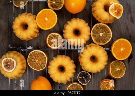 Kleine orange bundt Kuchen mit frischen und trockenen Orangen auf Kühlung ruck, Ansicht von oben, flach, horizontal Komposition Stockfoto