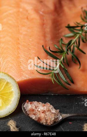 Roher Lachs filet auf schwarzem Schiefer Platte und Zutaten für die Herstellung von Graved Lachs. Salz, Zucker, Zitrone und Rosmarin im Hintergrund für trockene Heilung Marinade, da Stockfoto