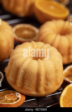 Kleine orange bundt Kuchen mit frischen und trockenen Orangen auf Kühlung ruck, Ansicht von oben, flach, vertikale Zusammensetzung Stockfoto