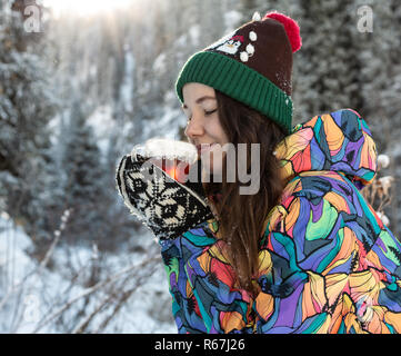 Mädchen genießt den Schnee fällt. Junge Frau in Form gestrickt ist Tee trinken im Wald bei einem Schneefall. Getönten Foto. Stockfoto