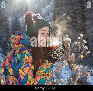 Mädchen genießt den Schnee fällt. Junge Frau in Form gestrickt ist Tee trinken im Wald bei einem Schneefall. Getönten Foto. Stockfoto