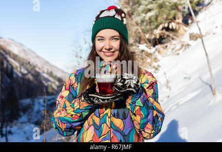 Mädchen genießt den Schnee fällt. Junge Frau in Form gestrickt ist Tee trinken im Wald bei einem Schneefall. Getönten Foto. Stockfoto