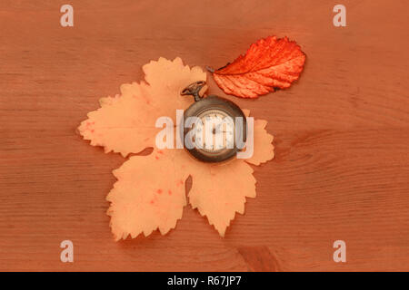 Eine alte Taschenuhr mit Herbstlaub, geschossen von oben auf einen dunklen Holzmöbeln im Landhausstil Hintergrund mit Kopie Raum, Sepia getont Bild Stockfoto