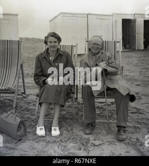 1950er Jahre, Histrocial, einem Briten, ein Mann und eine Frau tragen Röcke sitzen auf den Liegestühlen an einem Sandstrand, vor Veränderung oder Kurhaus-kiosken, England, UK. Stockfoto