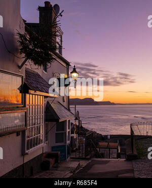 Lyme Regis, Dorset, Großbritannien. 4. Dezember 2018. UK Wetter: Ein herrlicher goldener Sonnenaufgang an der malerischen Stadt Lyme Regis als Morgendämmerung bricht über Golden Cap und der Jurassic Coast auf einer kalten und klaren Dezember Morgen. Die lebendige, farbenfrohe und Himmel ist in den Fenstern des historischen Gebäude der Stadt wider. Credit: Celia McMahon/Alamy leben Nachrichten Stockfoto