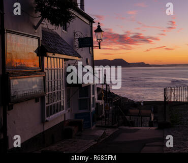 Lyme Regis, Dorset, Großbritannien. 4. Dezember 2018. UK Wetter: Ein herrlicher goldener Sonnenaufgang an der malerischen Stadt Lyme Regis als Morgendämmerung bricht über Golden Cap und der Jurassic Coast auf einer kalten und klaren Dezember Morgen. Die lebendige, farbenfrohe und Himmel ist in den Fenstern des historischen Gebäude der Stadt wider. Credit: Celia McMahon/Alamy leben Nachrichten Stockfoto