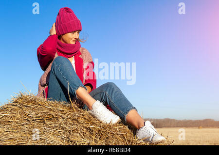 Mode lifestyle Portrait von jungen trendigen Frau in warmen stilvollen Fell gekleidet, Stricken hat und Jeans posiert und lächelnd auf Gelb ein Stapel von Heu. p Stockfoto