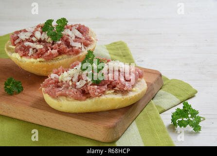 Brötchen mit Hackfleisch Wurst aus Schweinefleisch, deutschen zwiebelmettwurst mit Zwiebeln und Petersilie garnieren auf ein Frühstück, grüne Serviette und weißen Holzmöbeln bac Stockfoto