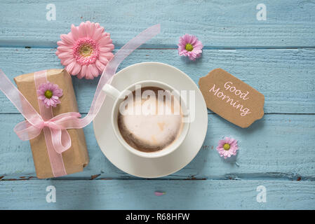 Kaffeetasse, rosa Blüten und ein Geschenk auf Pastell-blaue Holz Hintergrund mit Kopie Raum, text Guten Morgen, Draufsicht von oben Stockfoto