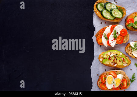 Satz frischer Toast Sandwiches mit Gemüse, gekochte Eier, Käse, Avocado, mit Gruenen und Gewürzen auf Stück steigen Papier und Vie serviert dekoriert Stockfoto