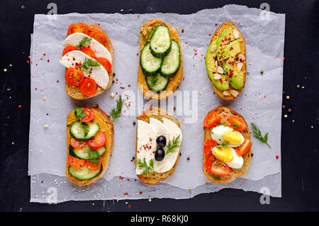 Satz frischer Toast Sandwiches mit Gemüse, gekochte Eier, Käse, Avocado, mit Gruenen und Gewürzen auf Stück steigen Papier und Vie serviert dekoriert Stockfoto