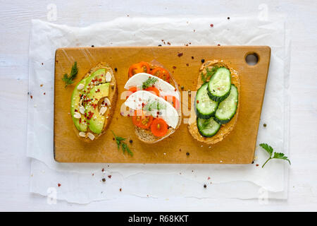 Satz von frischen Sandwiches mit Gemüse auf dunklem Brot, auf Holz Schneidebrett mit Grüntönen gehalten und Gesehen von oben Stockfoto