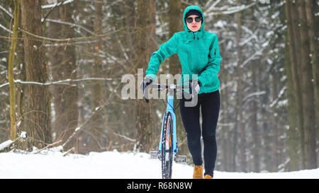 Radfahrer Frau geht mit dem Fahrrad auf dem Fahrrad in den verschneiten Wald in winterWinter Training im Freien Konzept Wanderwege Stockfoto