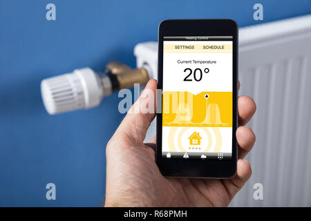 Person Festlegen der Hand Temperatur Thermostat mit Mobilephone Stockfoto