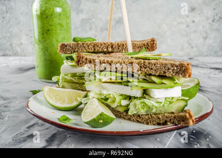 Vegane Snacks oder Mittagessen, gesunde Sandwiches mit Avocado und Mehrkornbrot, am grauen Stein Hintergrund mit grünem Gemüse Smoothie, Platz kopieren Stockfoto