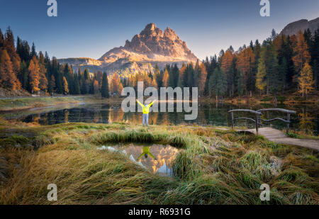 Mann mit erhobenen Waffen auf Antorno See mit Reflexion der Tre Cime di Lavaredo bei Sonnenaufgang im Herbst in den Dolomiten, Italien. Landschaft mit glücklichen Menschen, Gr Stockfoto